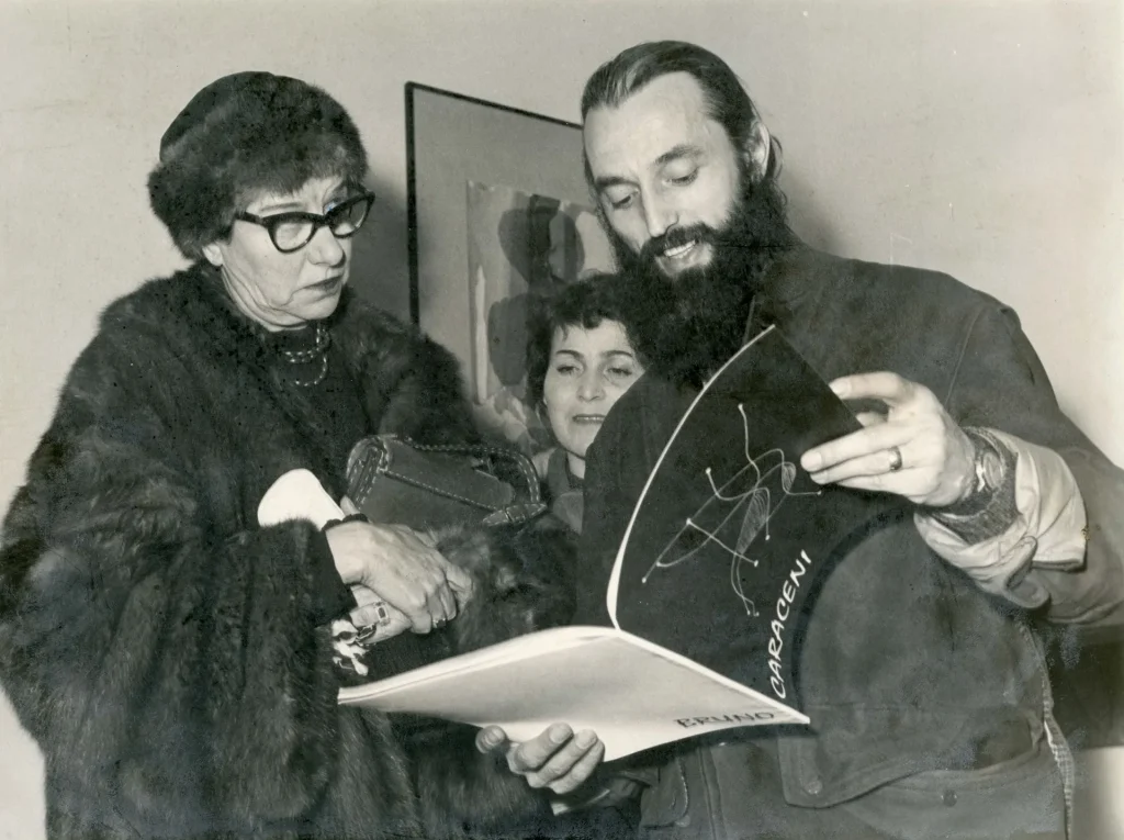 immagine per Peggy Guggenheim in visita alla Galleria Appia Antica di Roma nel 57 guarda il catalogo di B. E. Caraceni